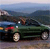 Green convertible car with red taillight, white headlights, and silver wheels on a road with blurred background