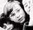 Black-and-white pixelated image of a person with dark hair, wearing a high-collared garment and holding an object near the face.