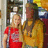 Two people stand side-by-side in a room with shelves; the person on the left wears red, and the right wears yellow. Text appears below them.