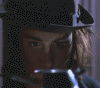 A four- shows a person in dark clothing with light brown hair and a black hat, holding a metallic object near their face