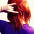A person with long red hair and a purple top makes a hand gesture near their head, viewed from behind.