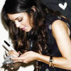 A woman with long dark hair wearing a sleeveless dark top holds a small object in her hands.