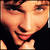 Pixelated close-up of a person's face with warm skin tones, dark hair, and a black garment visible at the bottom right.