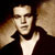 Static 50x50 pixel buddy icon showing a close-up of a person's face with dark hair and a black jacket over a white shirt, rendered in low-resolution pixel art style against a gradient background.