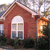 A pixelated image of a red brick building with an arched window and a small orange structure on the right side, set against a blurred background.