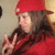 A person wearing a red cap and red jacket makes a peace sign with their right hand against a light-colored background.