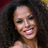 A woman with voluminous curly hair smiles broadly, showing teeth; the image appears in a