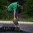 A person in a green shirt and blue pants performs a skateboarding trick on a ramp, with text elements on a green background.