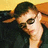 Pixelated image of a person with dark hair wearing sunglasses, hand raised near face against warm-toned background.