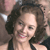 Pixelated close-up of a person with dark curly hair wearing a black strap top, smiling with visible teeth and pink lips against a blurred background.