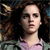 Pixelated image of a person with curly brown hair wearing a light purple top against a dark background with blurred brown and blue tones.