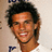 Pixelated close-up of a person with dark curly hair, light brown skin tone, and visible teeth in a smiling expression against a neutral background.