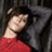 Pixelated image of a person with dark hair wearing a red top against a dark background with gray vertical elements.