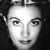 Black-and-white pixelated close-up of a human face with dark hair, neutral expression, and visible eyes, nose, and mouth against a dark background.