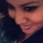 A person with dark hair and light skin smiles slightly, wearing a dark top against a blurred background.