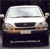 A white sedan with brown accents on the front bumper and headlights, viewed from a low angle against a dark background.