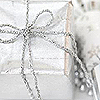 A static image of a white gift box with a silver ribbon tied in a bow, partially wrapped in white fabric with a subtle pattern.
