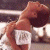 A pixelated image of a person with brown hair wearing white clothing, holding an object near their face against a blurred background.