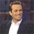 Pixelated image of a person with light skin tone wearing a white collared shirt and dark jacket against a dark background.
