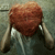 A heart-shaped red object with textured surface held by two hands against a gray background, showing subtle motion changes across frames.