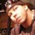 Pixelated image of a person with light skin tone wearing dark clothing, holding a light-colored object near their face.