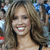 A static pixelated image shows a person with long brown hair, light skin, and a smiling expression, wearing a dark strap over one shoulder.
