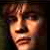 Pixelated close-up of a person's face with warm lighting and dark background, showing partial facial features including eyes, nose, mouth, and hair in low-resolution style.