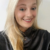 Pixelated portrait of a person with long blonde hair wearing dark clothing against light background.