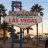 Pixelated static image of a signpost with multiple directional signs against a sunset sky, featuring palm trees and blurred background elements.