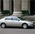A silver sedan with blue-tinted windows is parked on a street in front of a building with columns and greenery.