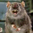 Pixelated image of a light brown animal with rounded ears, dark eyes, and a dark nose, positioned against a blurred background with blue and green tones.