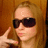 A static pixelated image shows a person with light brown hair wearing dark sunglasses, holding a phone to their ear against a wooden background.