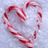 A heart-shaped arrangement of red-and-white striped candy canes on a light textured surface, with blue background containing pixelated text and emoticons