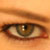 A close-up of a human eye with brown iris and visible eyelashes, set against warm-toned skin tones in pixelated detail.
