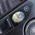 Pixelated circular icon with iridescent gradient on dark background, featuring light blue, green, and pink hues in a blurred, low-resolution style.