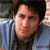 A pixelated close-up of a person with dark hair wearing a blue striped shirt against a blurred background.