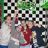 Four people pose together in front of a black-and-white checkered background with green foliage above, while blue text lists names on the right and a blue arrow symbol appears below.