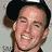 Pixelated close-up of a person wearing a dark cap, smiling with visible teeth, against a light background.