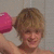 A static image shows a person with light brown hair holding a pink object near their head against a neutral background.