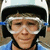 A person wearing a white helmet with black straps and clear goggles, blue shirt visible at collar, neutral expression.