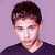 Static pixelated image of a person with short dark hair wearing a dark shirt against a light purple background.