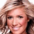Pixelated close-up of a person with light brown wavy hair, smiling face showing visible teeth, and dark eyes against a white background.