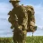 Pixelated image of a person in dark clothing holding a large brown object against a blue sky and green field background.