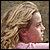Two side-by-side profile images of characters with long hair, one in pink clothing and the other in dark clothing against a grassy background.