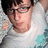 A pixelated image of a person with dark hair and glasses wearing a white shirt, set against a teal background with pixelated text.