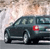 Static image of a dark-colored sedan viewed from the side, positioned on a road with a blurred background of light and brown tones.