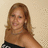 A pixelated static image shows a person with long light brown hair wearing a black top with white patterns against a beige background.
