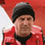 Pixelated image of a person wearing a dark beanie and red jacket with black collar against red background.