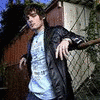 A person in a black jacket and light blue shirt stands outdoors near a fence, with text reading 'he is mine.' and 'BACK to the —>OFF' below.