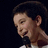 Pixelated image of a person with short dark hair holding a microphone, split into four quadrants with red text on black and gray backgrounds.